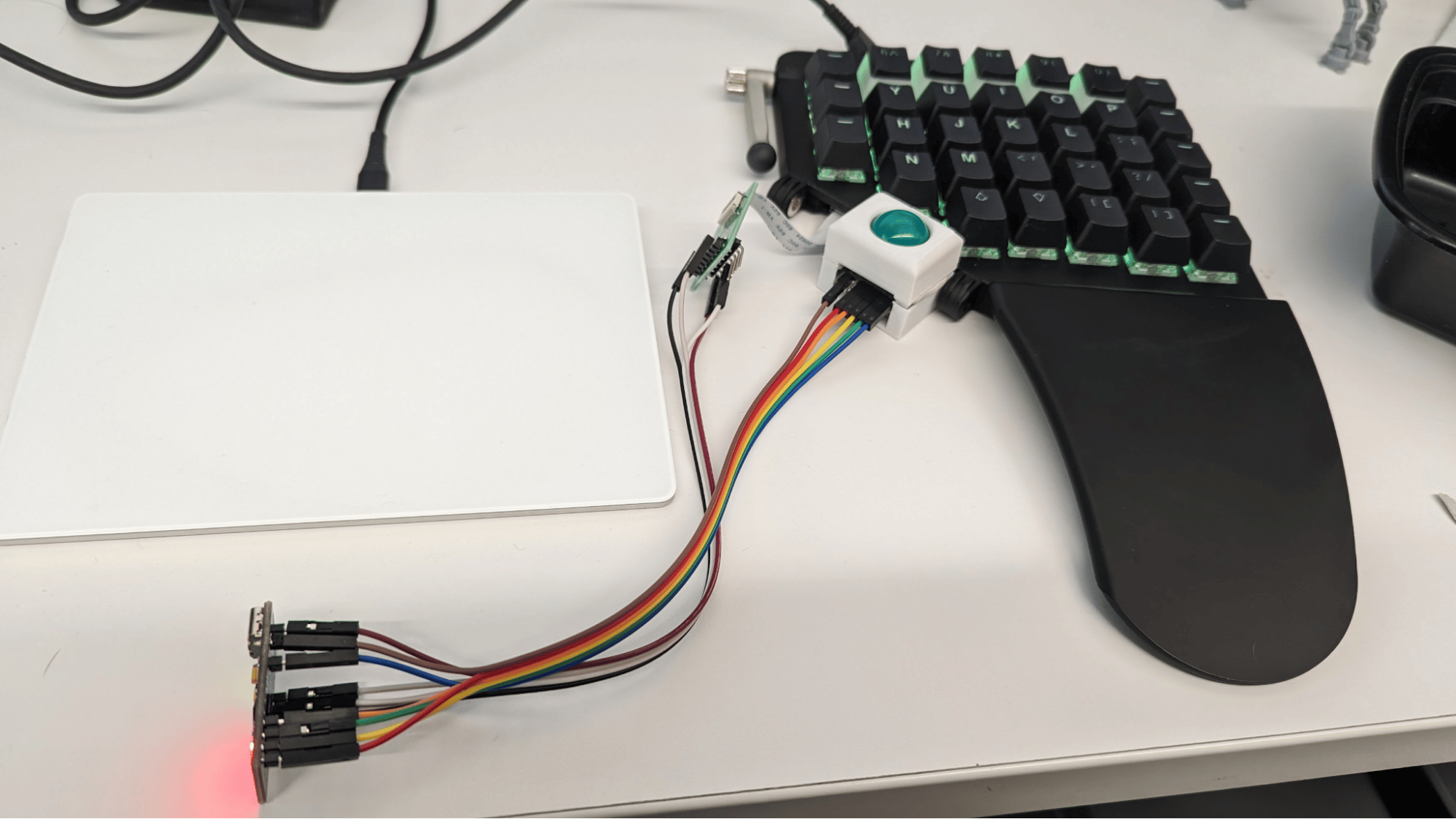 A picture of an early prototype of the Moonrover. The right trackpad for the Moonlander is completely gone, and in it's place is a trackball housing with a bunch of wires running to a microcontroller, which then has a bunch of wires running back to a ribbon cable breakout board, which is connected to the keyboard.